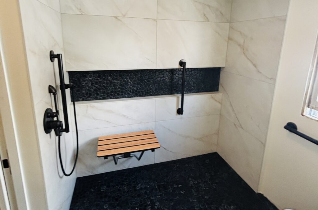 Walk-in shower with large-format tile, a mosaic accent band, teak bench, and grab bars by Royal Kitchen & Bathroom Remodels.